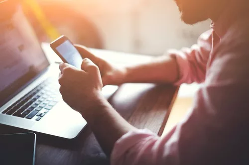 man using phone in front of computer