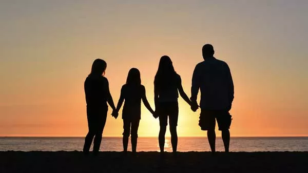 a family of four holding hands by the ocean looking toward the sunset
