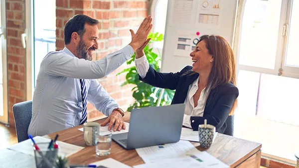 two team members high fiving at an office desk