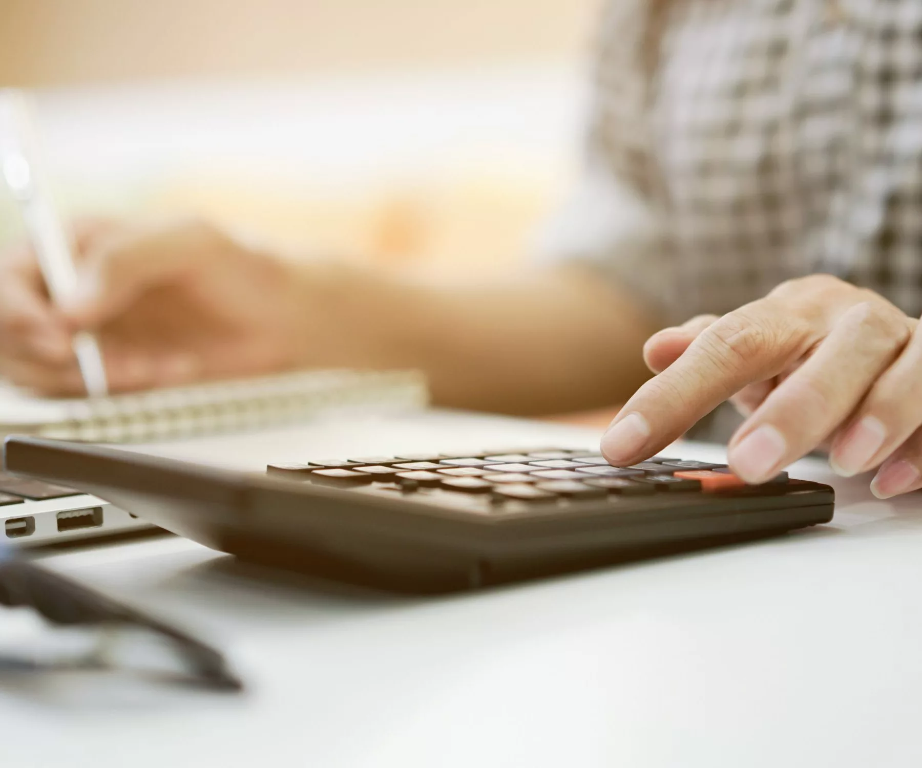 person using a calculator and notepad in front of laptop