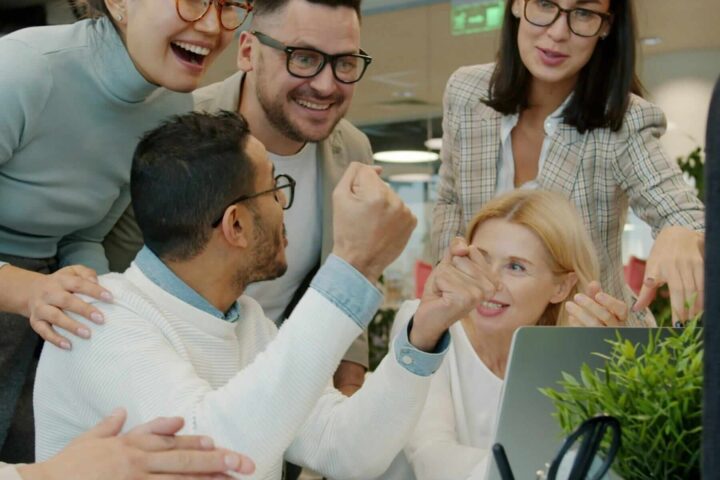 five coworkers happily looking at something exciting on laptop screen