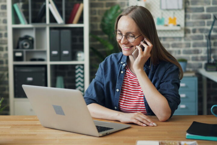 woman talking on phone in front of laptop computer